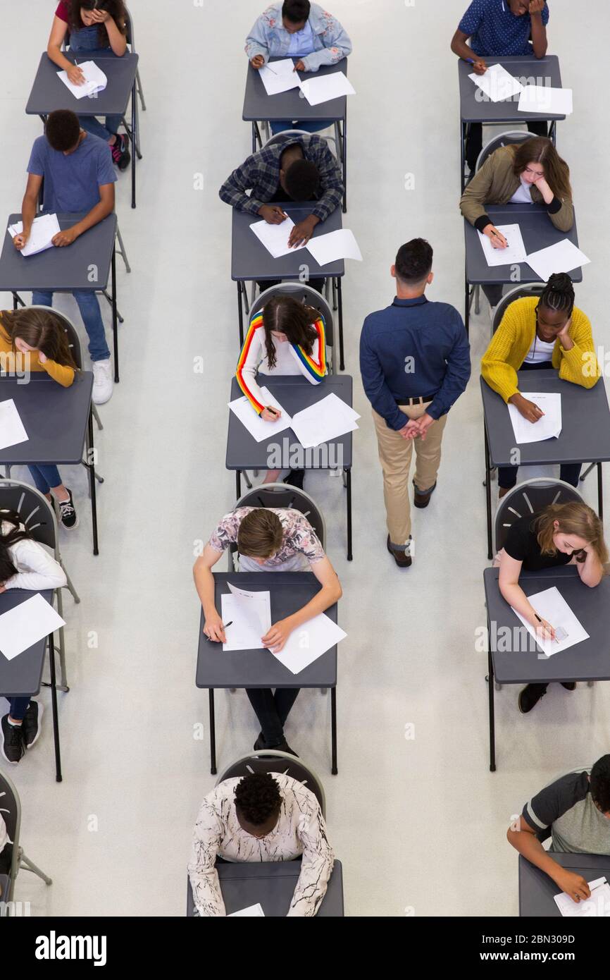 Lehrer überwacht High School Studenten, die Prüfung an Schreibtischen Stockfoto