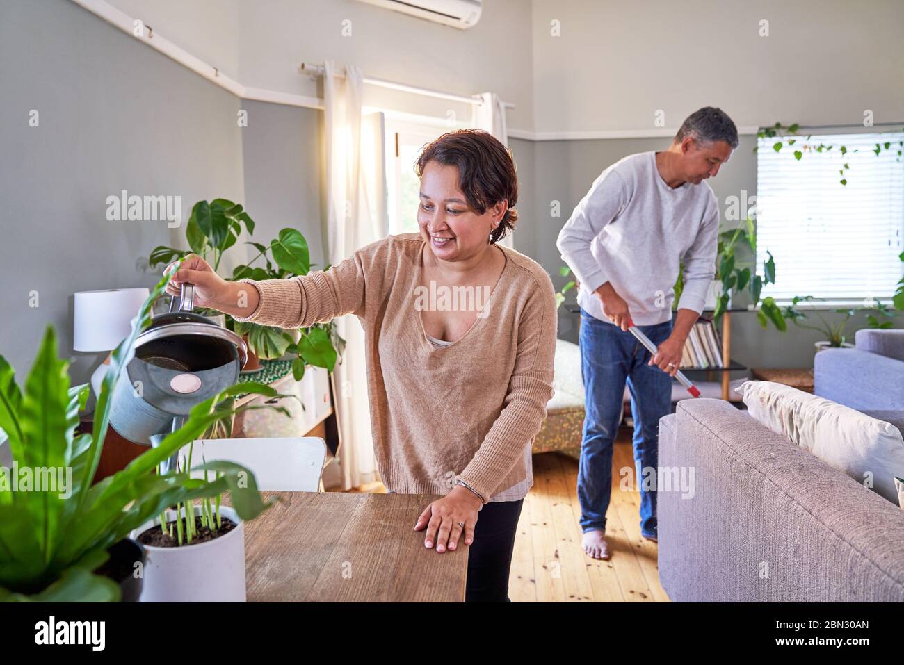 Älteres Paar Bewässerung Zimmerpflanzen und Reinigung Wohnzimmer Stockfoto