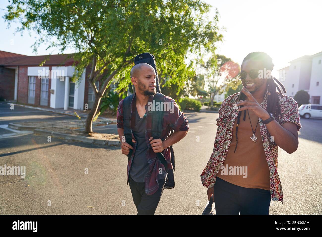 Männliche Musiker mit Gitarrenkoffer zu Fuß auf sonnigen Straße Stockfoto