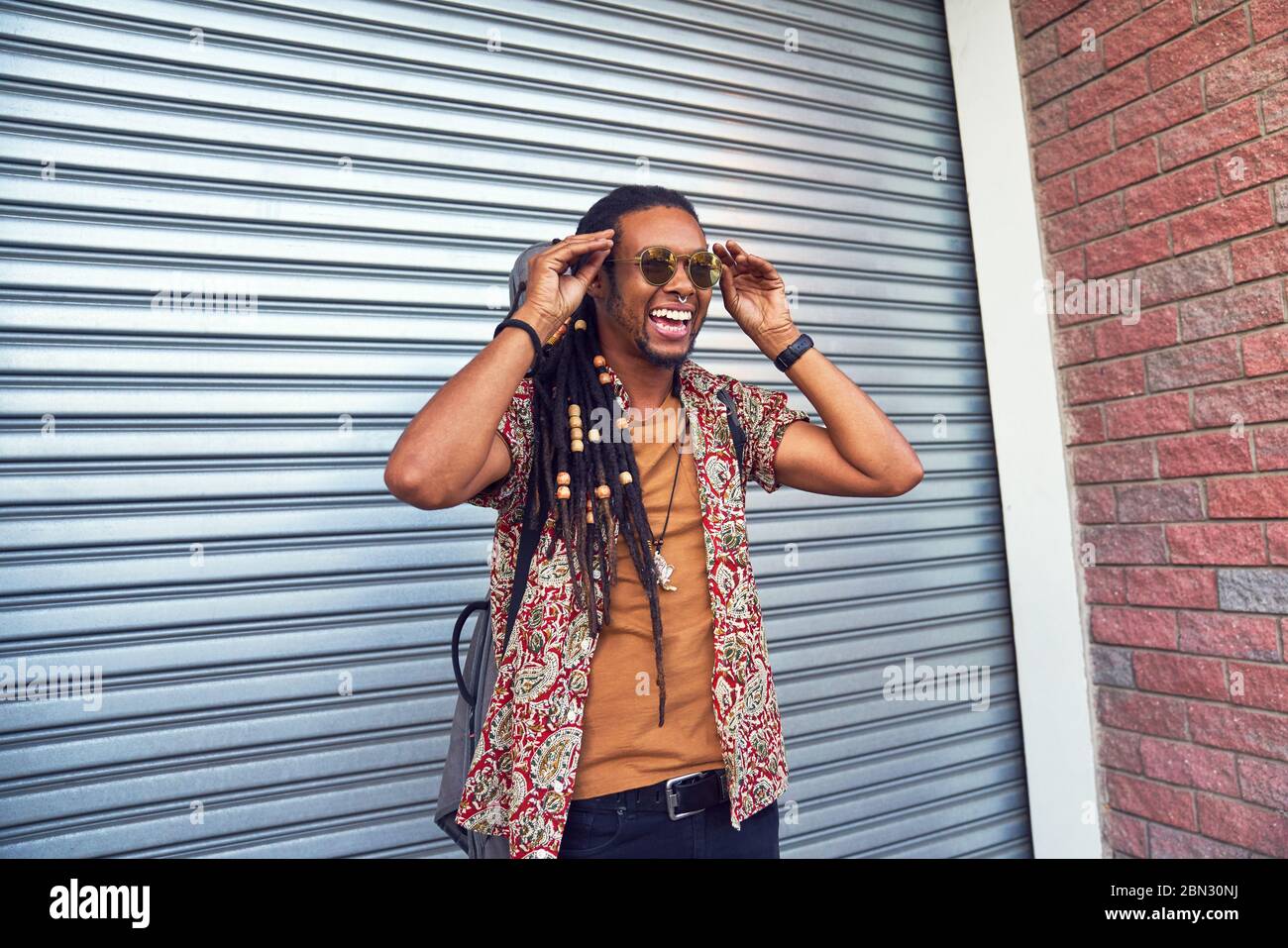 Fröhlicher Mann mit Dreadlocks und Sonnenbrille außerhalb der Garage Stockfoto