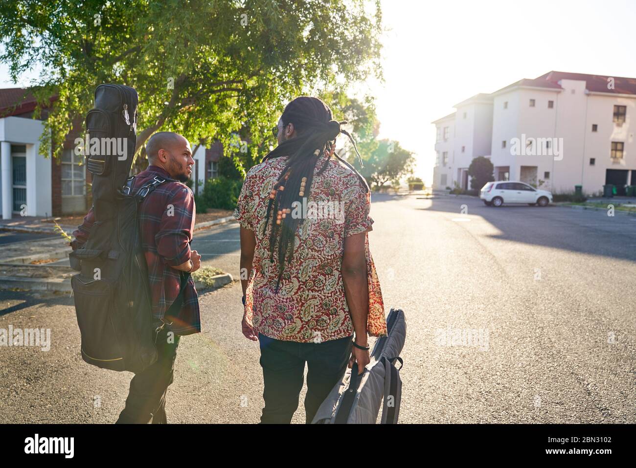 Männliche Musiker mit Gitarrenkoffer, die auf der sonnigen Straße spazieren Stockfoto