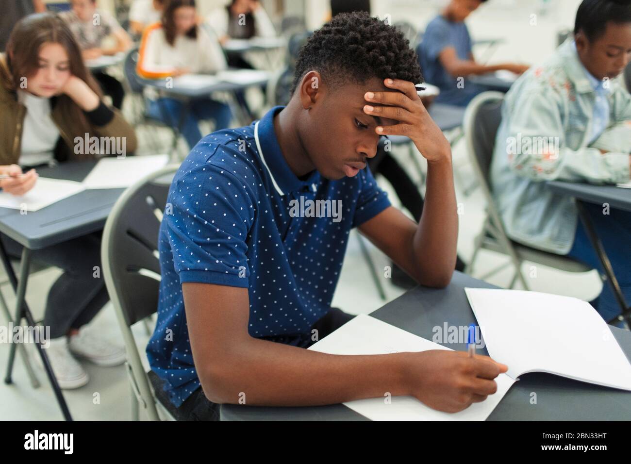 Fokussierter High School Junge, der Prüfung am Schreibtisch im Klassenzimmer nimmt Stockfoto