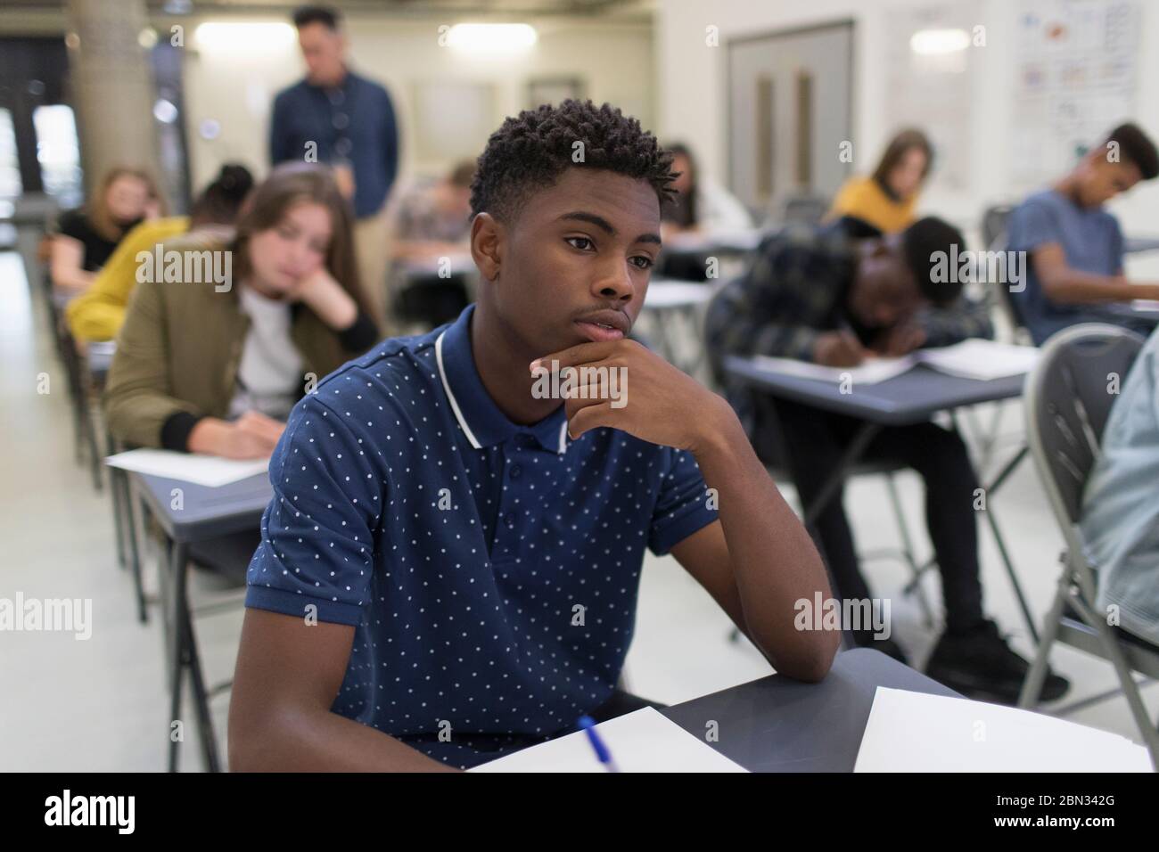 Nachdenkliche High School junge, die Prüfung am Schreibtisch im Klassenzimmer Stockfoto