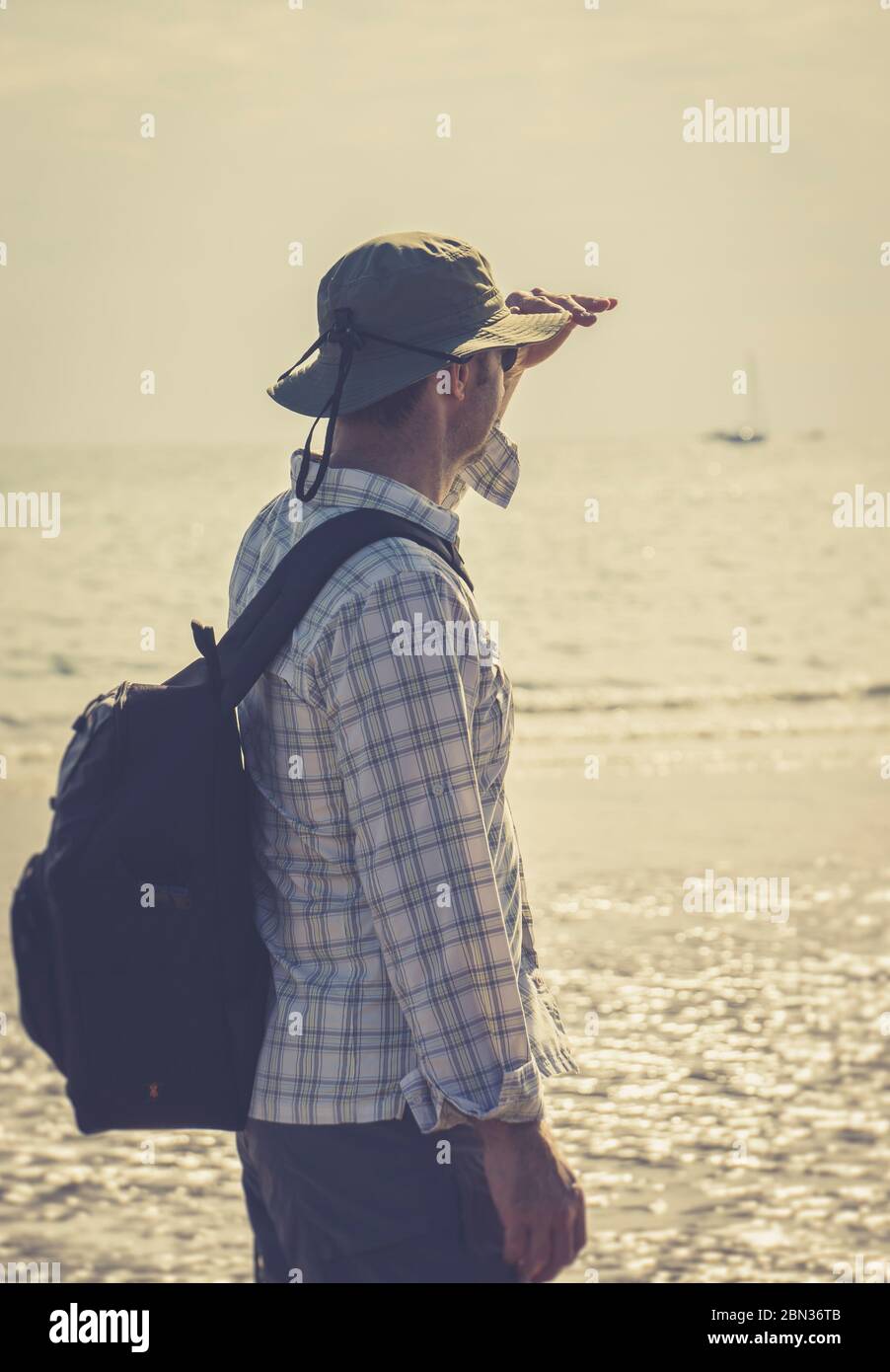 Rückansicht Nahaufnahme eines isolierten britischen Urlauters mit Sonnenhut am britischen Strand mit Blick auf das Meer. Sommerurlaub Aufenthalt, Mann schützt die Augen. Stockfoto