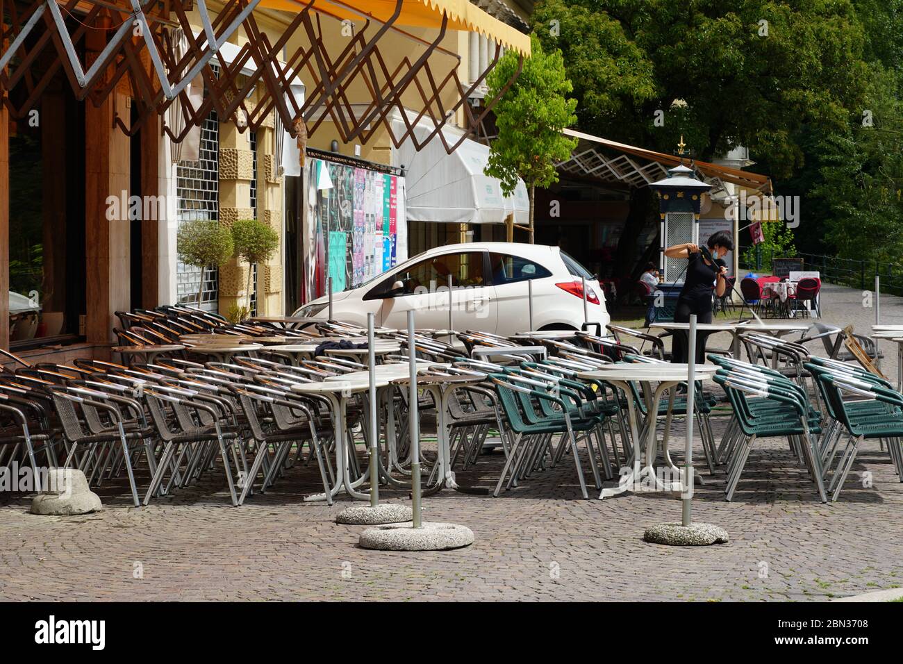 Italienische Restaurants in Meran, Südtirol, sind wegen COVID-19 noch geschlossen. Stühle und Tische stehen gestapelt und verkettet. Dame, die putzt Stockfoto