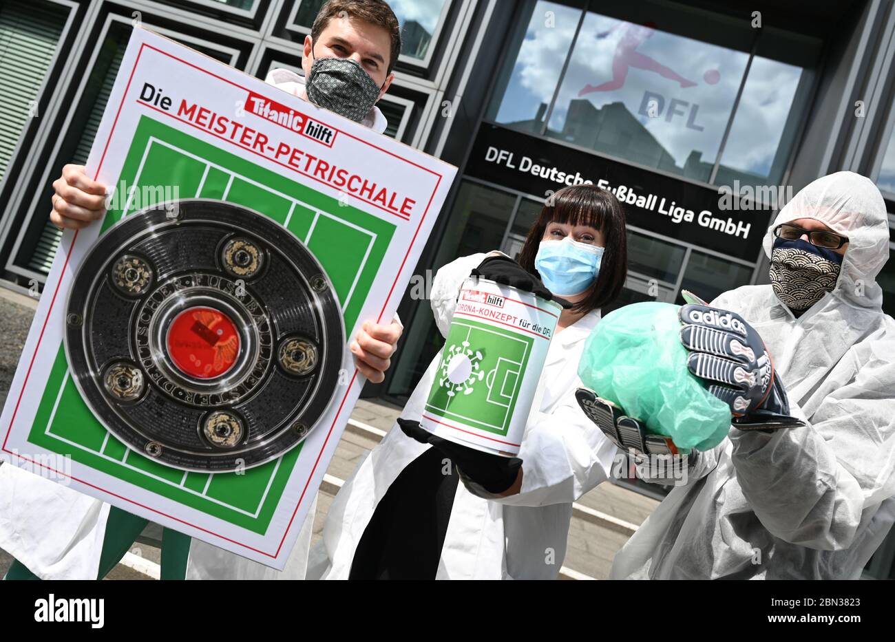 12. Mai 2020, Hessen, Frankfurt Am Main: Chefredakteur Moritz Hürtgen (l.), Martina Werner und Torsten Gaitzsch von der Satirezeitschrift 'Titanic' tragen Gesichtsmasken bei der Präsentation der 'Master Petri Dish', einer 'Torona Spendenbox' und eines 'Hygieneballs mit doppelter Haardecke' während einer Kampagne vor dem Hauptquartier der Deutschen Fußball-Liga (DFL). Die 'Titanic'-Redakteure wollten ihr '11 11'-Konzept für den sicheren Spielbetrieb der DFL übergeben und präsentieren. Foto: Arne Dedert/dpa Stockfoto