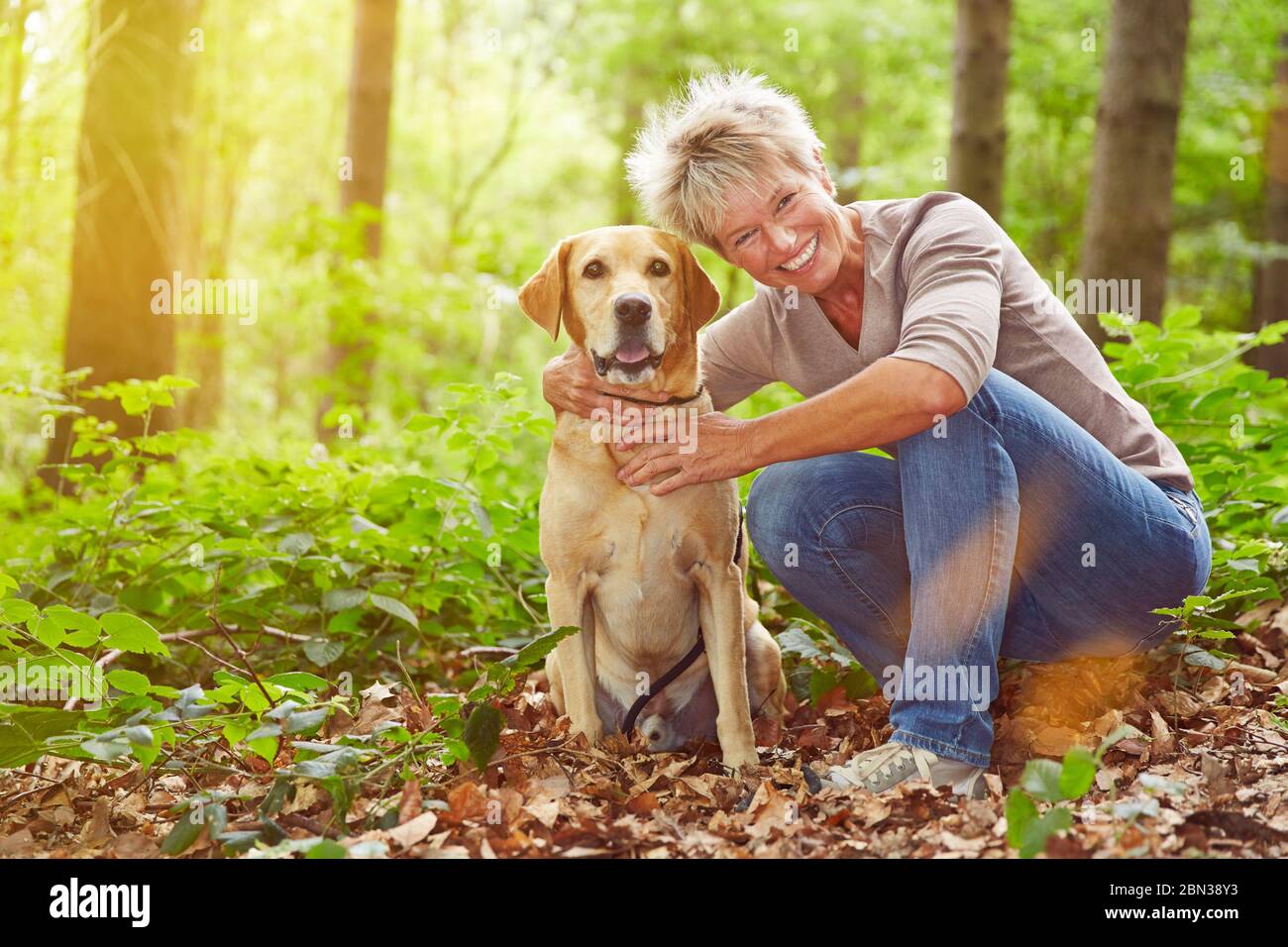 Ältere lächelnde Frau sitzt mit Hund im Wald Stockfoto