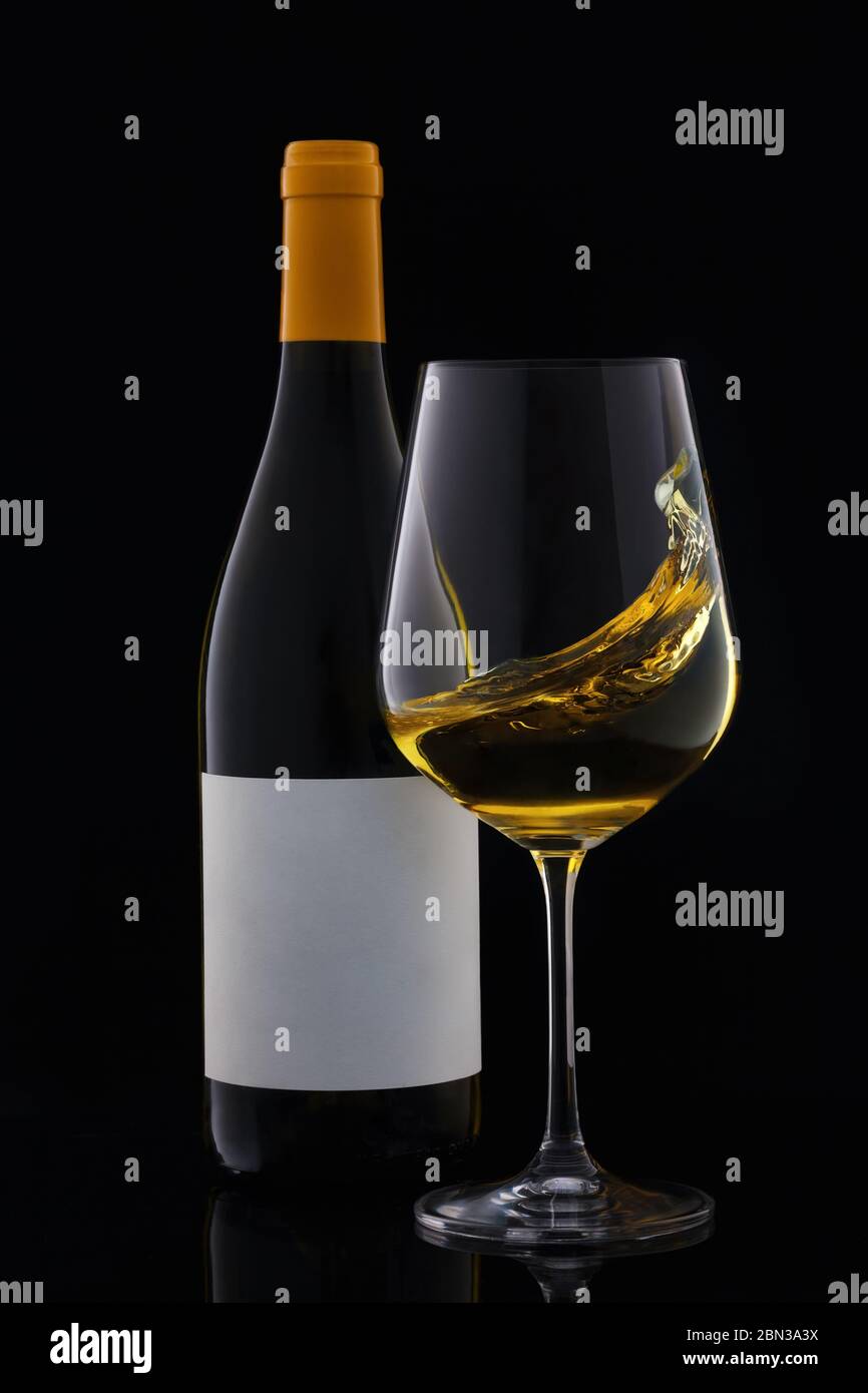 Weißweinflasche und Weinglas mit leerem Etikett isoliert auf schwarzem Hintergrund. Stockfoto