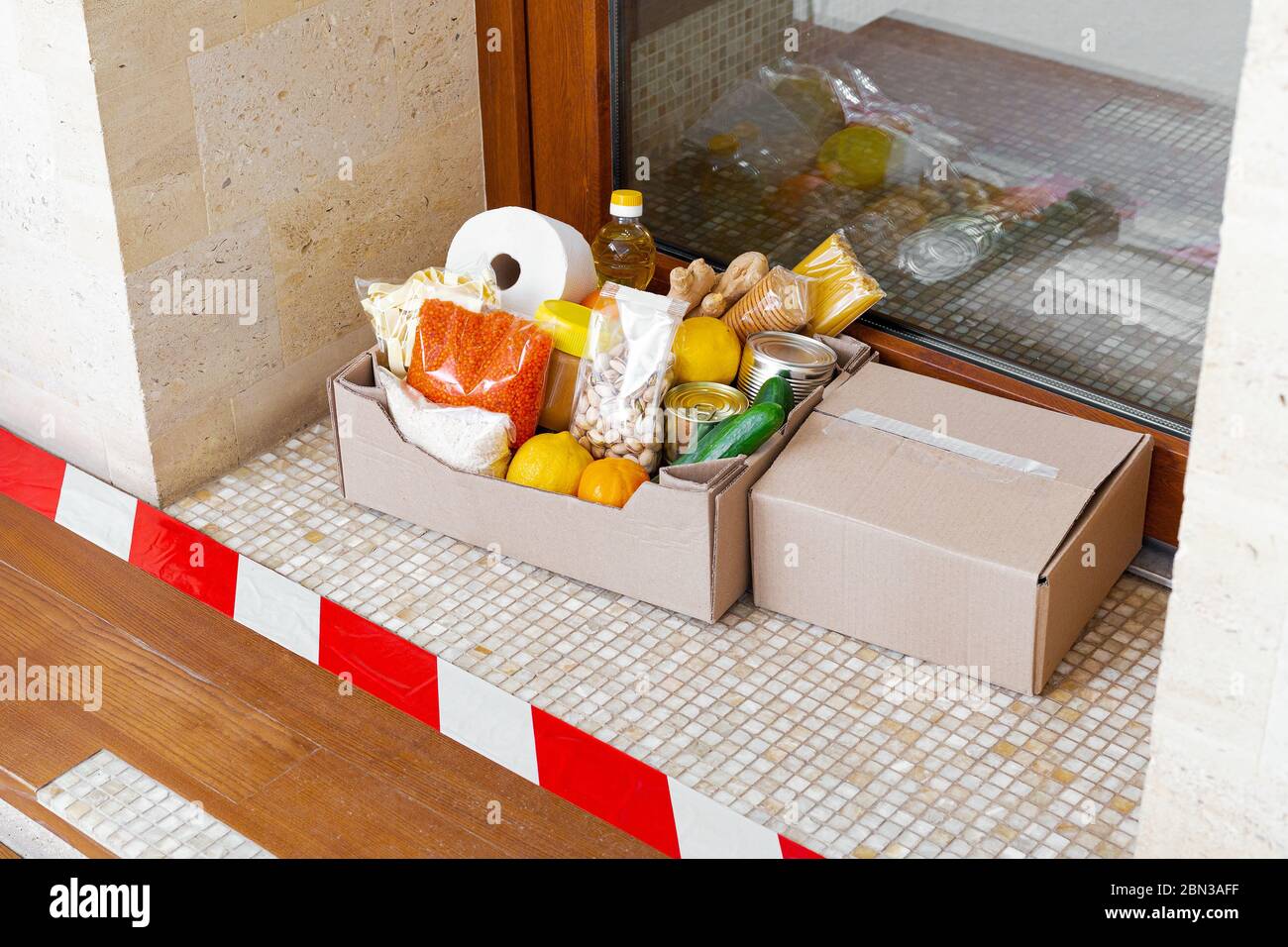 Box mit Lebensmitteln während der Selbstisolation covid Quarantäne zu Hause. Die Lieferung der Foodbox vor der Tür hinter der Schlange. Kontaktlose Lieferung, sicher Stockfoto