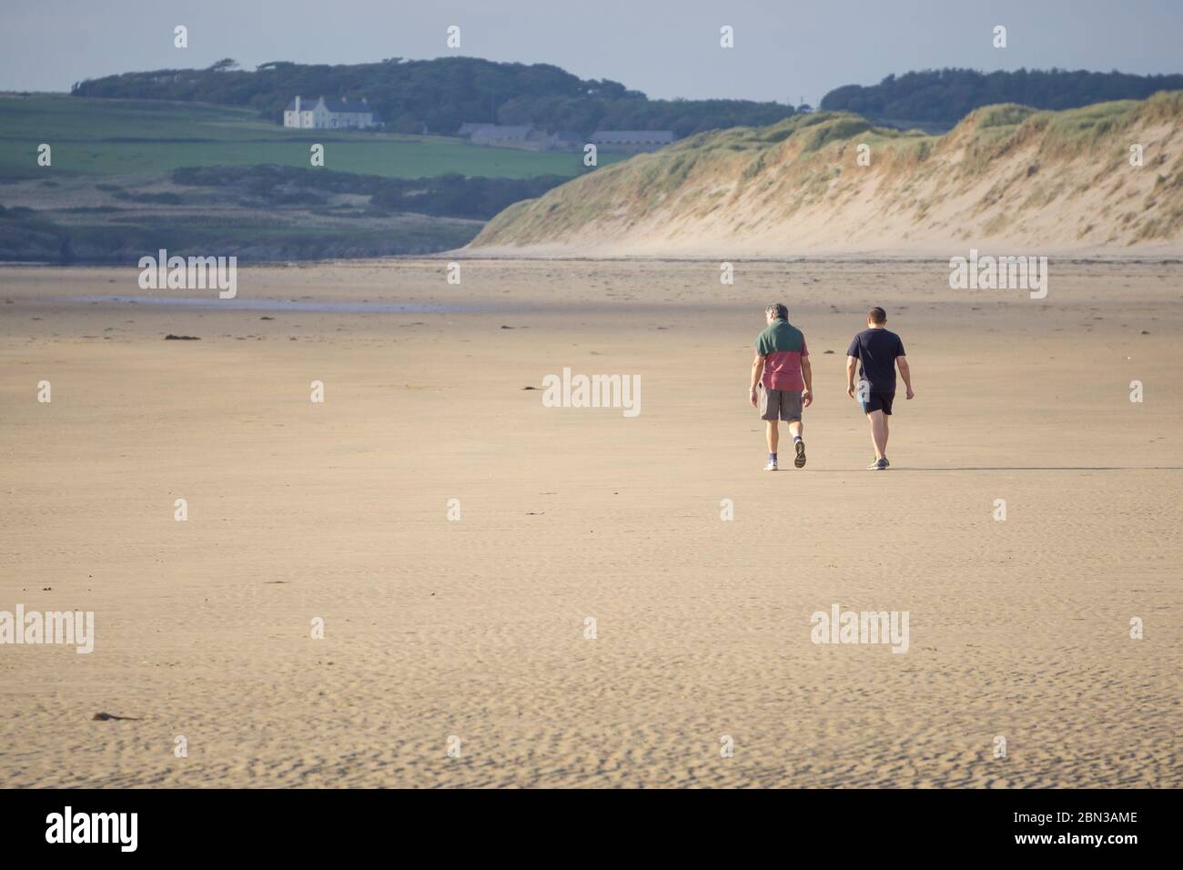 Isolation am leeren, menschenleeren Newborough Beach. Vater und Sohn gehen zusammen für die tägliche Bewegung auf isolierten britischen Strand. Sommerurlaub in Großbritannien. Stockfoto