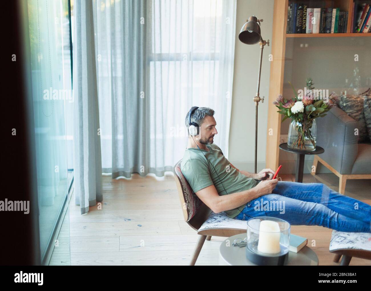 Mann, der sich im Wohnzimmer entspannt, Musik mit mp3-Player und Kopfhörer hört Stockfoto