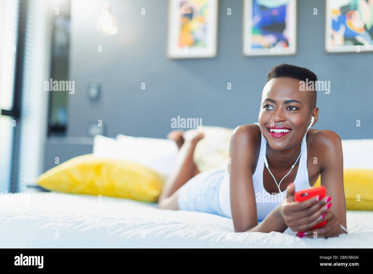 Lächelnde junge Frau, die sich auf dem Bett entspannt und Musik mit mp3-Player und Kopfhörern hört Stockfoto