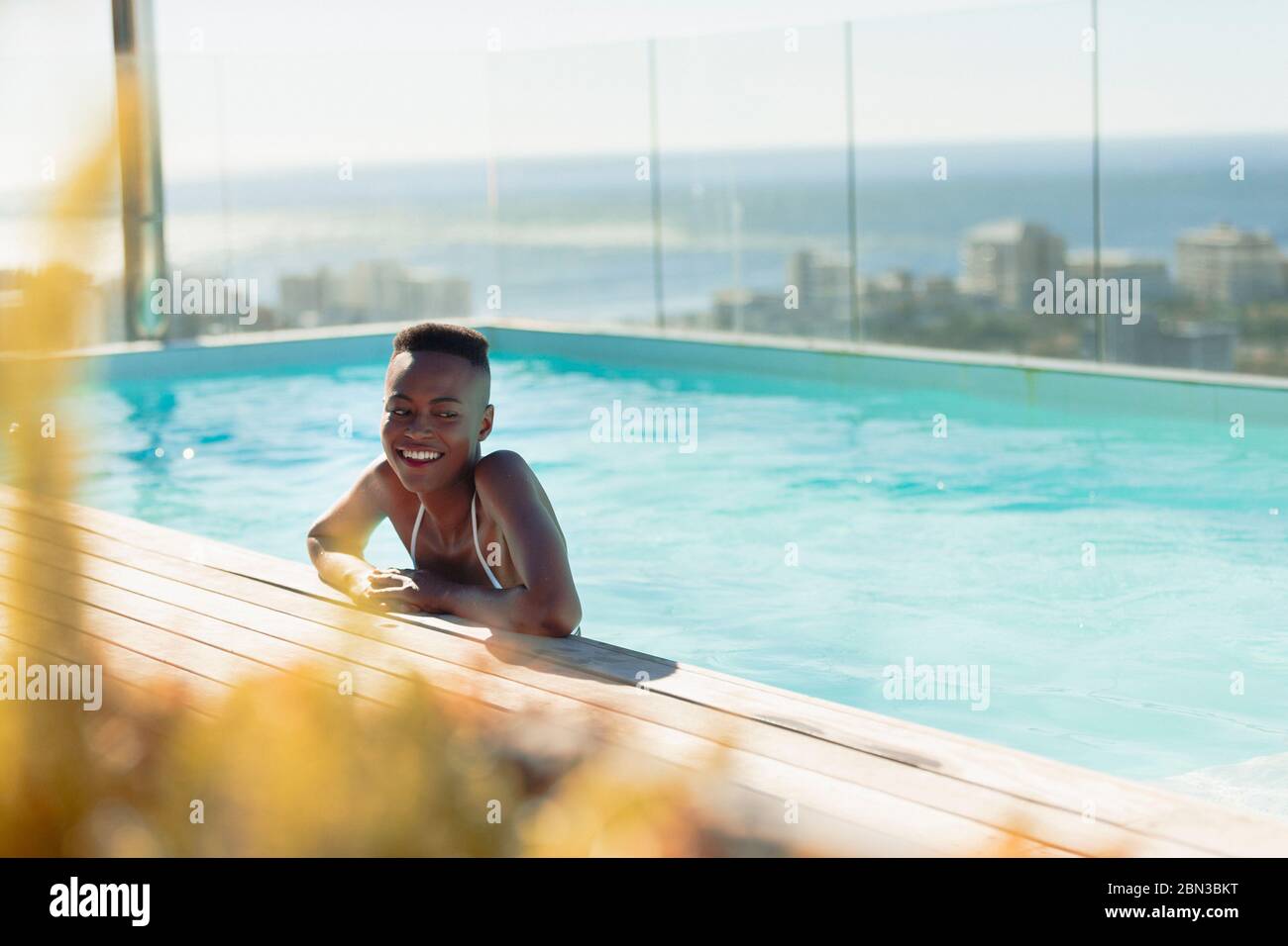 Glückliche junge Frau in sonnigen, luxuriösen Pool Stockfoto