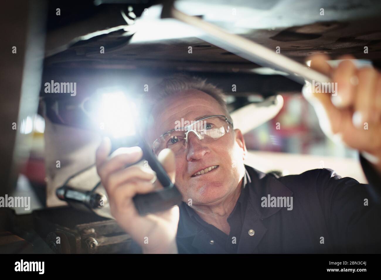 Männliche Mechaniker mit Taschenlampe arbeitet unter Auto in der Auto-Werkstatt Stockfoto