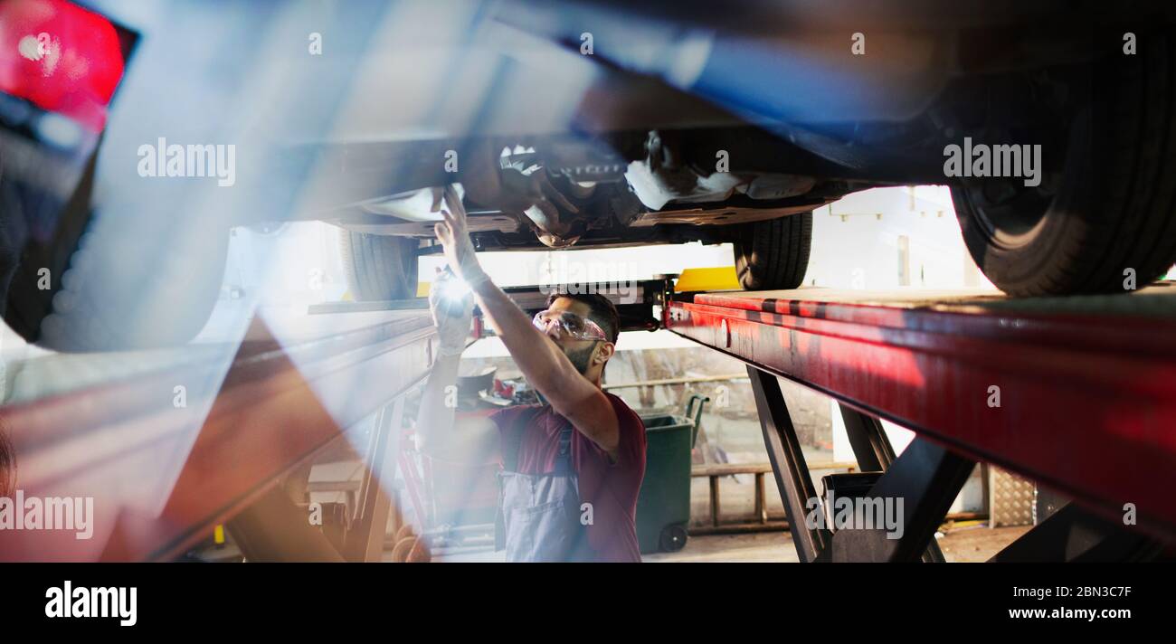 Männliche Mechaniker unter dem Auto in der Werkstatt arbeiten Stockfoto