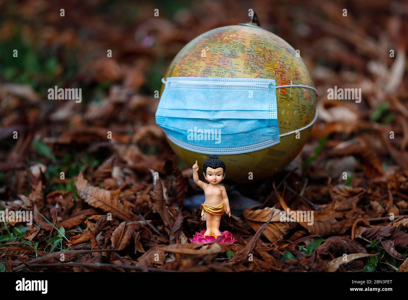 Coronavirus (COVID-19)-Epidemie. Blaue Einweg-Gesichtsmaske auf einem kranken Weltglobus und Buddha-Kind. Stockfoto