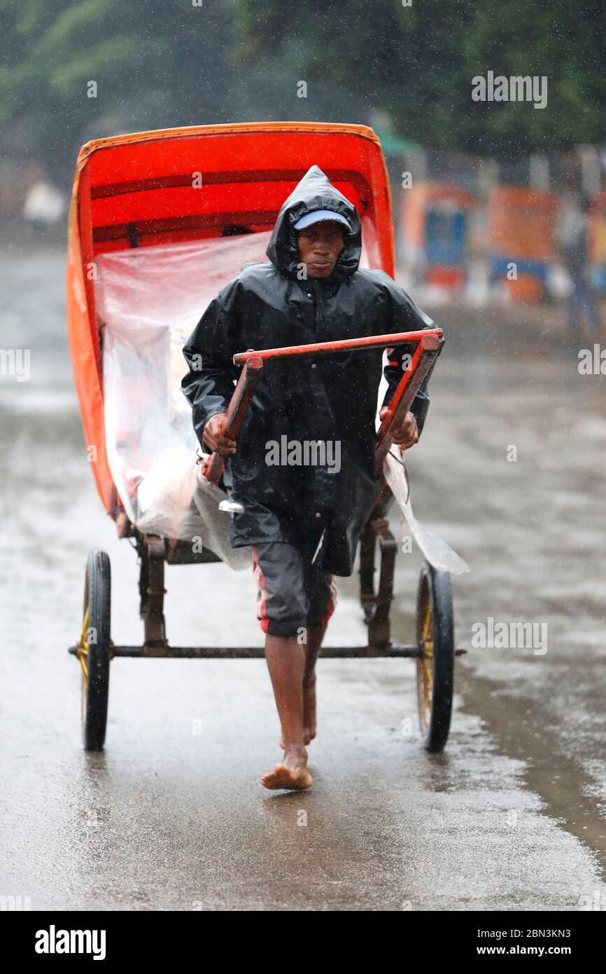 Pousse-Pousse (Rikscha) Fahrer bei starkem Regen. Antsirabe. Madagaskar. Stockfoto