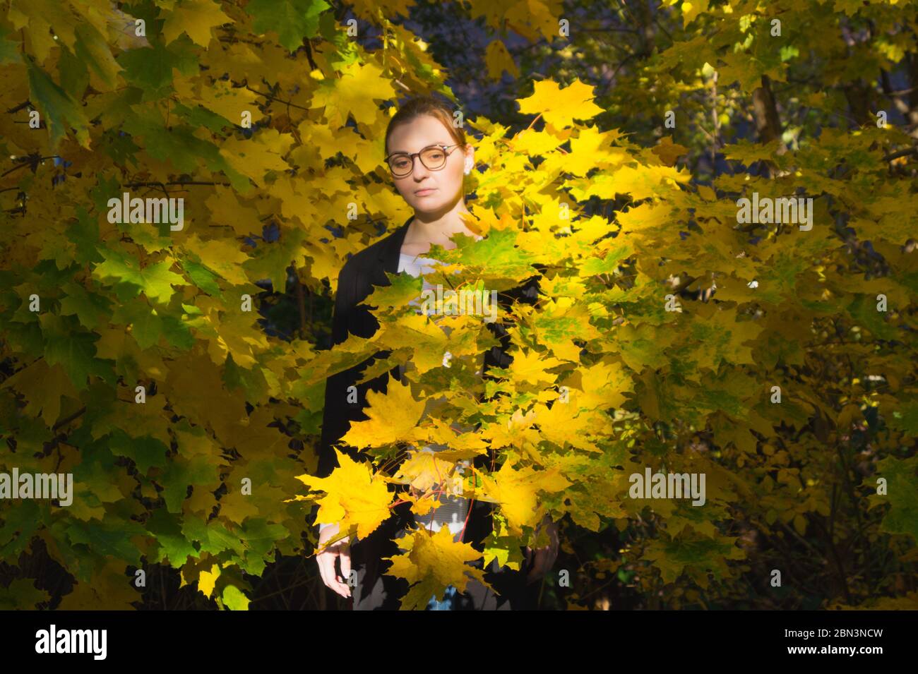 Eine Frau steht inmitten von leuchtend gelben und grünen Blättern und sieht traurig und nachdenklich aus. Mit dem Anflug des Winters ist sie von der Herbstangst beängstigt. Stockfoto