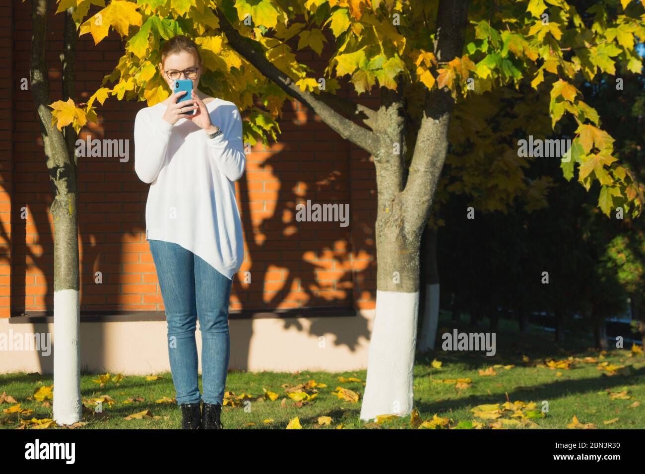 Eine junge Frau tippt, während sie ihr Telefon auf Augenhöhe hält. Dabei vermeidet sie den sogenannten Smartphone-Einbruch, der Schmerzen und Wunden verursacht. Stockfoto