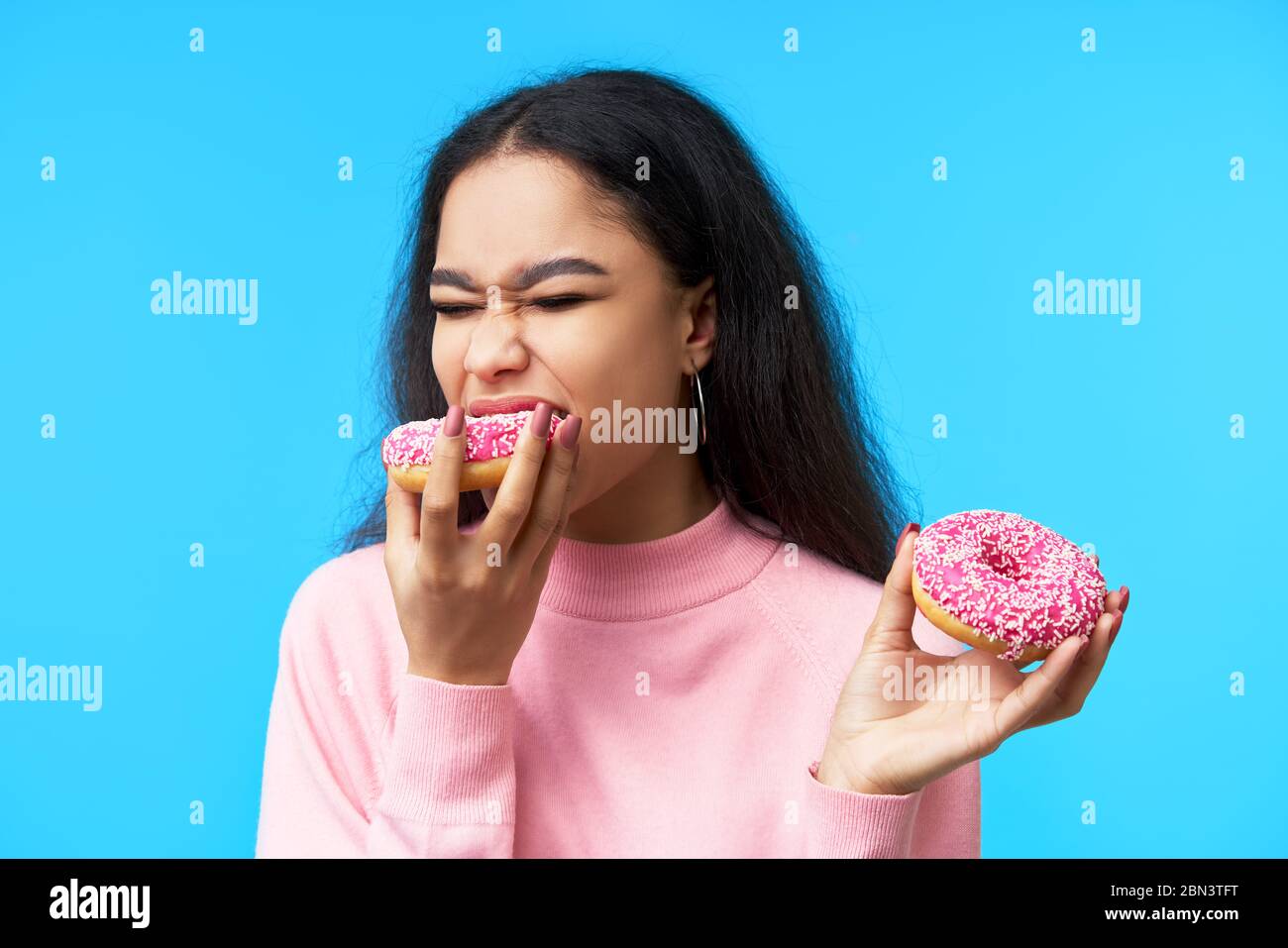 Hungrig hübsches Mädchen essen Donuts isoliert über blauem Hintergrund. Lecker, Versuchung Essen Stockfoto