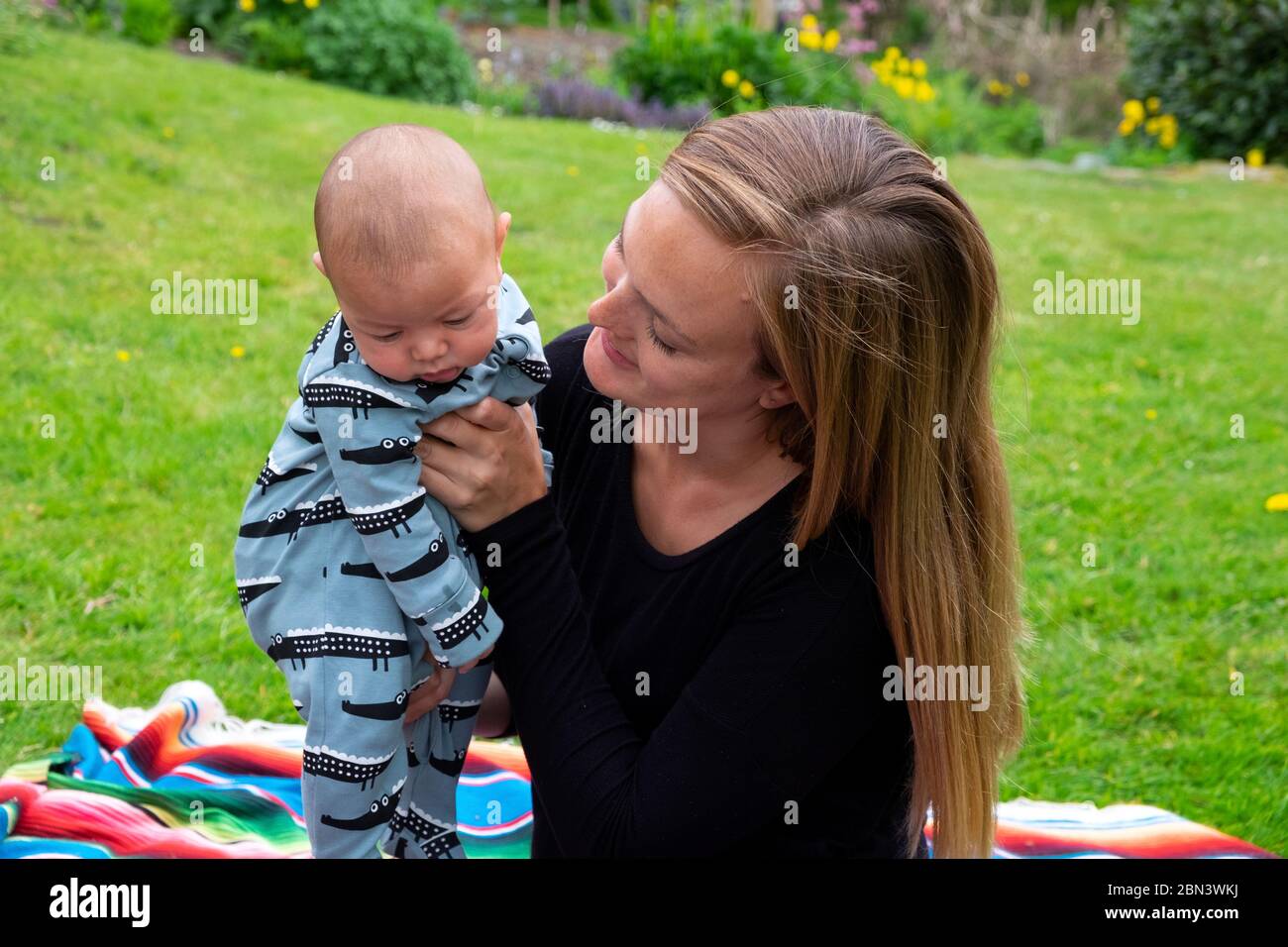 Leben in Lockdown covid 19 2020 für Mutter sitzen im Landgarten lächelnd bei 3 Monaten Baby Junge draußen im Mai Sonnenschein Wales UK KATHY DEWITT Stockfoto