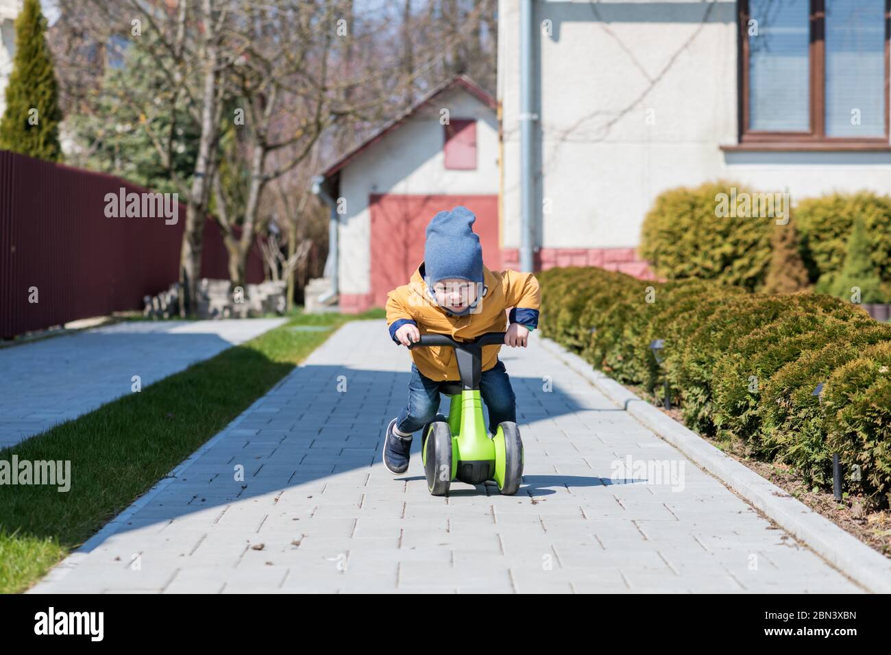 Kleiner Junge auf seinem Fahrrad auf Pflasterweg in der Nähe seines Hauses. Happy Kindheitkonzept Stockfoto