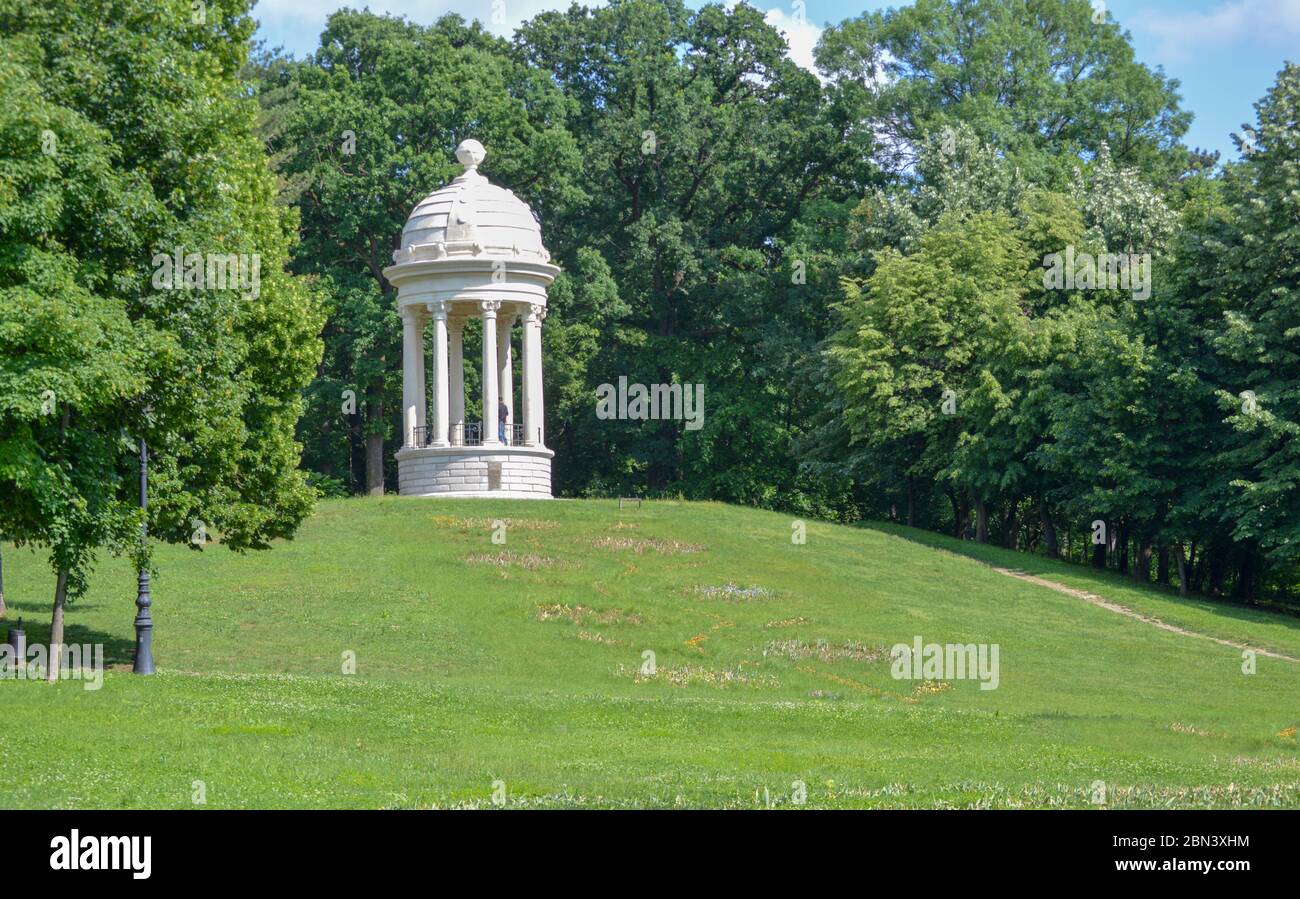 Ein weißer Marmorpavillon auf einem grasbewachsenen Hügel, umgeben von Bäumen am Eingang zum Nicolae Romanescu Park in Craiova, Rumänien, 3. Größter Naturpark in Stockfoto