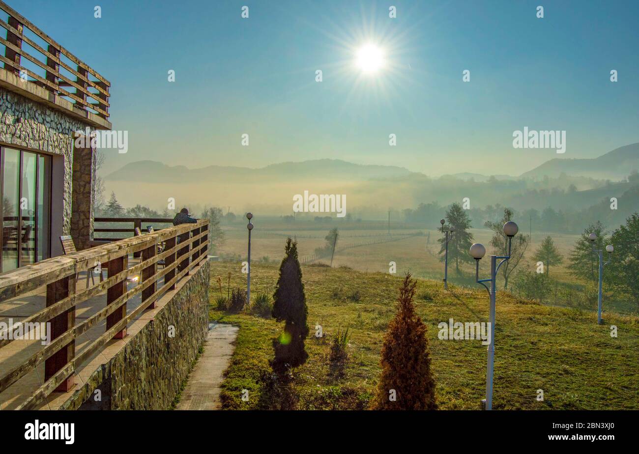 Eine ruhige Szene irgendwo in den rumänischen Bergen, eine ruhige Morgensonne über einer Holzvilla in einer Wiese, umgeben von Vegetation und Morni Stockfoto