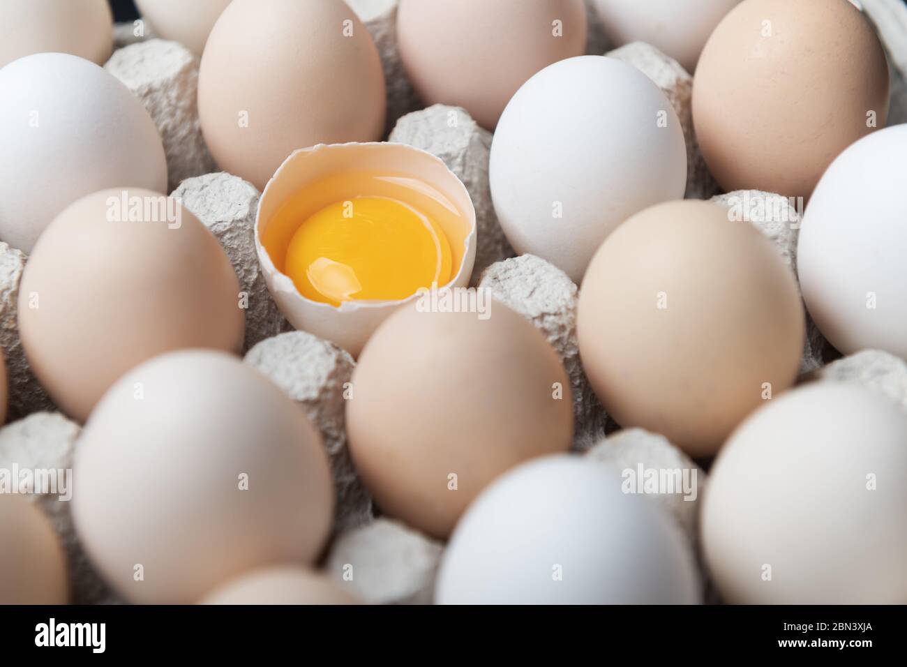 Hühnereier in Bio-Verpackung Nahaufnahme. Ei halb gebrochen unter anderen Eiern. Food-Fotografie Stockfoto