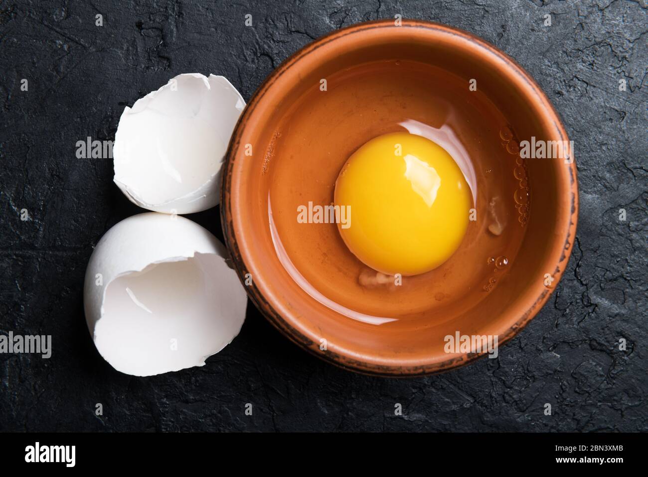 Hühnerdotter aus gebrochenem Bio-Ei in braunem Teller auf schwarzem Betongrund. Food-Fotografie Stockfoto