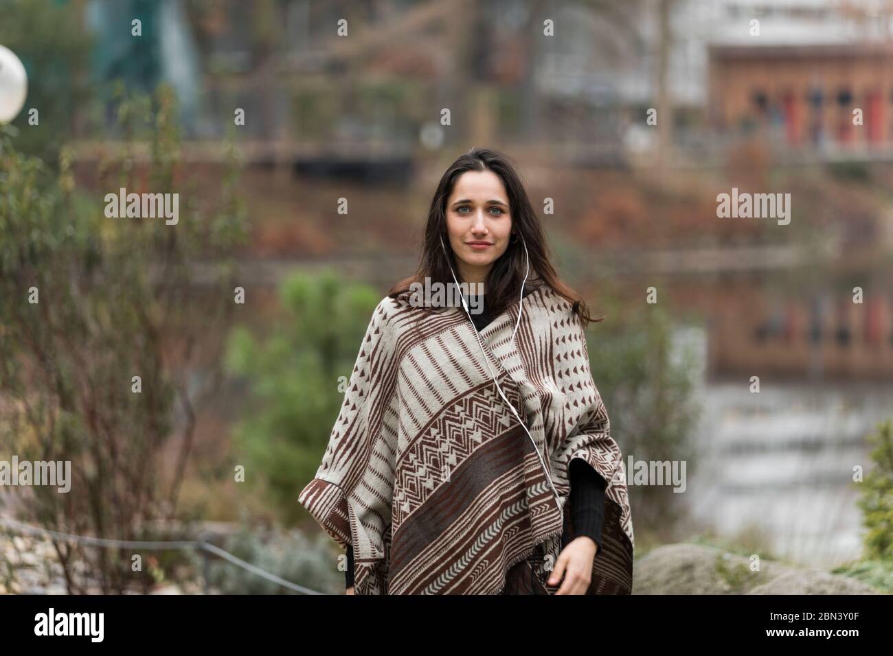Medium Shot von dunkelhaarigen weiblichen Modell posiert im Poncho im Freien. Vorderansicht. Stockfoto