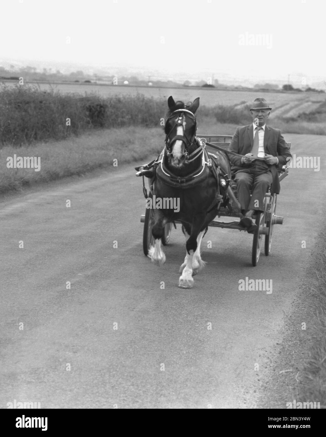 1980er Jahre, ein Reisender Gentleman in Anzug, Krawatte und Hut, reitet mit Pferd und Wagen auf einer offenen Landstraße, Yorkshire, England, Großbritannien. Stockfoto