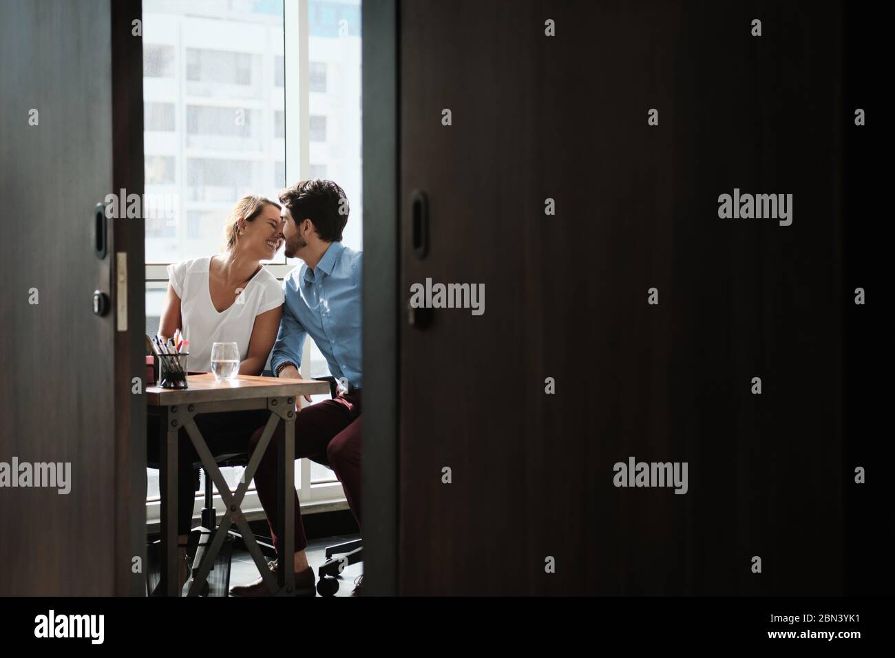 Zwei Mitarbeiter Sitzen Am Büroschreibtisch Und Küssen Stockfoto