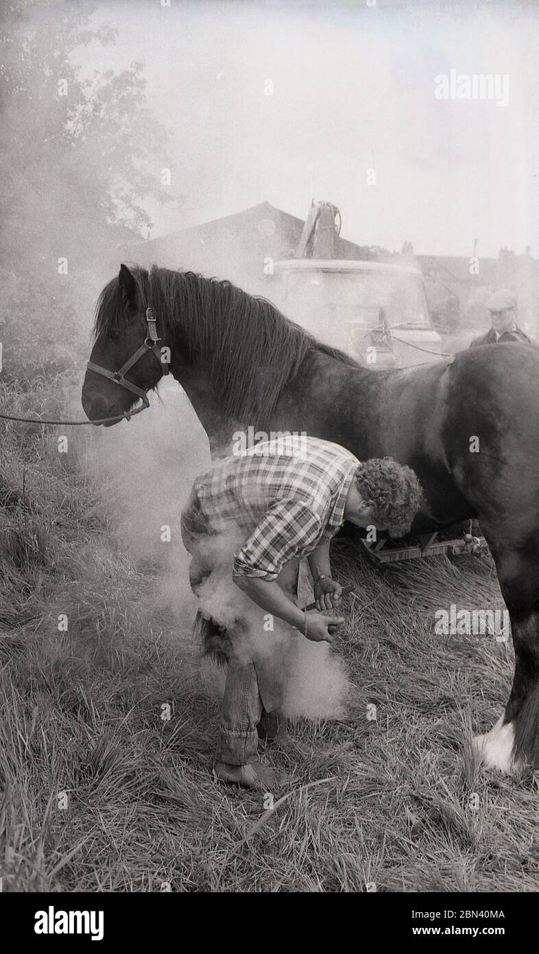 1987, heißes Shoeing..... Auf einer Zigeuner- oder Reisesternmesse steigt Dampf auf, während ein Farrier ein Pferd umhackt und es auf den Haufen legt, während es noch rot heiß ist, damit es an einem Ort brennt, an dem es richtig passt, England, Großbritannien. Stockfoto