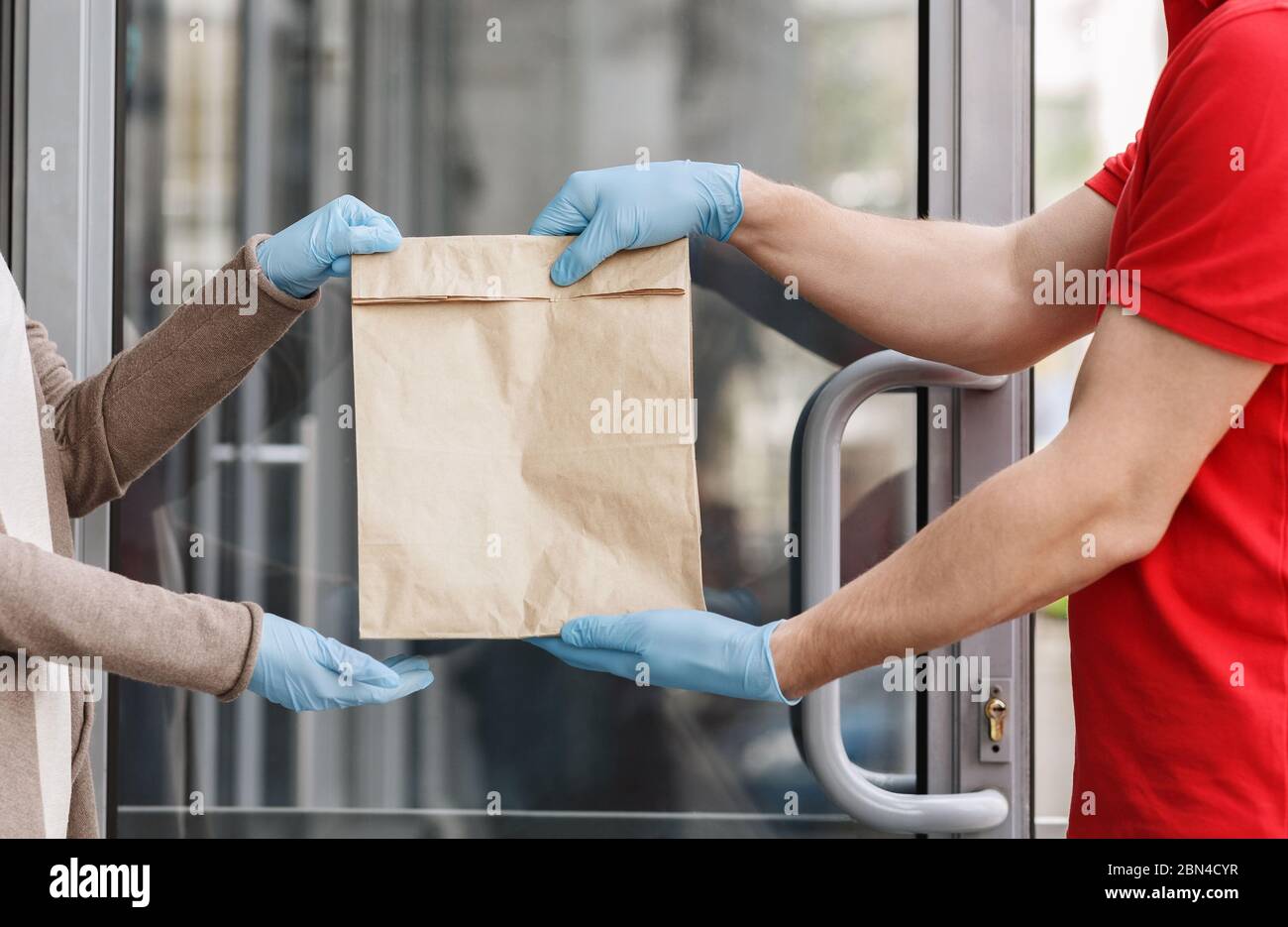 Kurier in Gummihandschuhen liefert Papiertüte an Kunden zu Hause. Stockfoto