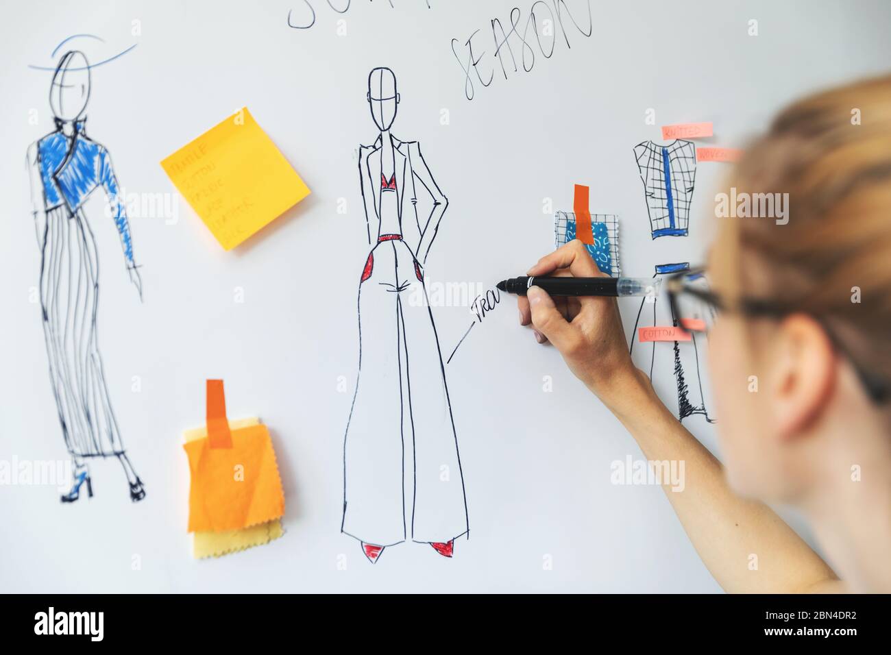 Modedesignerin skizziert neue Bekleidungskollektion auf Whiteboard Stockfoto