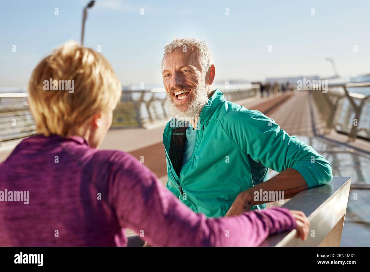 Nach dem Morgen laufen. Fröhlicher reifer bärtiger Mann in Sportkleidung, der mit seiner Frau spricht und am Morgen auf der Brücke lächelt Stockfoto