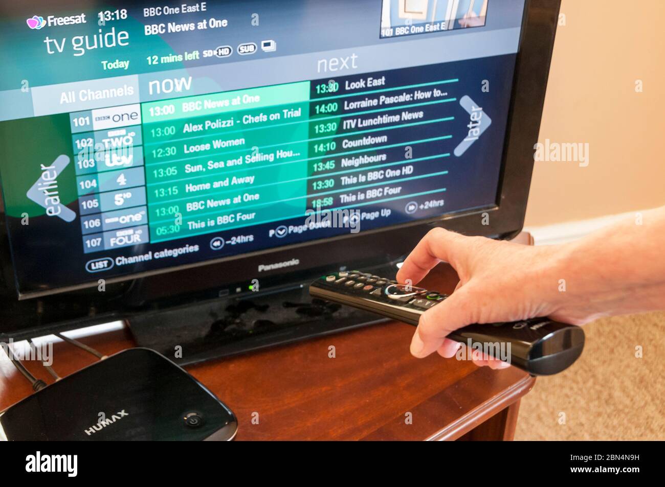 Frau, die eine Fernbedienung verwendet, um über eine Humax Set-Top-Box auf den Freesat TV Guide zuzugreifen. Stockfoto