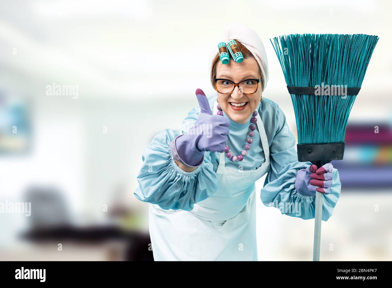 Porträt einer Putzfrau mit einem Putzbesen in den Händen. Eine Putzfrau in Uniform steht gegen ein helles Büro. Stockfoto