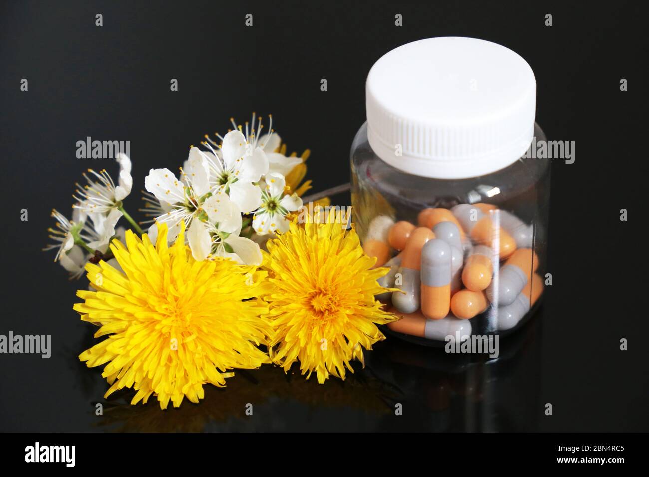 Pillen in einer Flasche und frischen Frühlingsblumen, Medikamente in Kapseln auf einem dunklen Glastisch. Konzept der Kräutermedizin, Apotheke, natürliche Vitamine Stockfoto