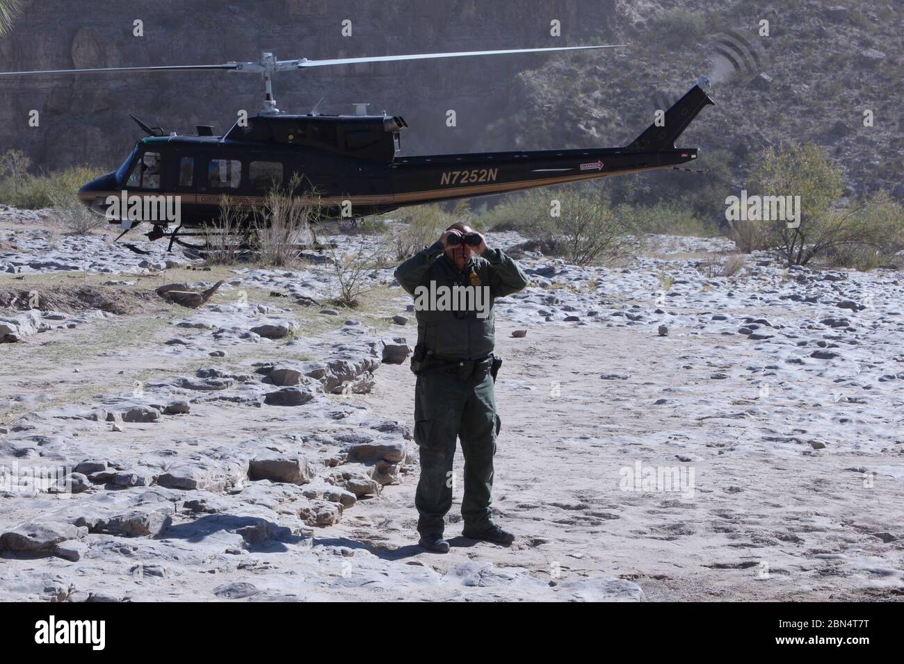 US-Grenzschutzagent Lance Van Buren verwendet Ferngläser, um interessante Gebiete entlang des Rio Grande zu beobachten, während ein US-amerikanischer Zoll- und Grenzschutz-Air and Marine Operations-Zweig UH-1N Hubschrauber im Hintergrund im Leerlauf 6. Dezember 2019. Der Agent im Feld wurde von der Alpine Air-Einheit unterstützt, die unter die AMO-Niederlassung El Paso Air fällt. Big Bend Sektor umfasst über ein Viertel der südlichen Grenze der Vereinigten Staaten und die Verwendung von Hubschraubern für Flugmobilitätsoperationen zu bewegen Grenzpatrouillen Agenten und Lieferungen in und aus den Gebieten raues Gelände erhöht Befürchtungen und Stockfoto