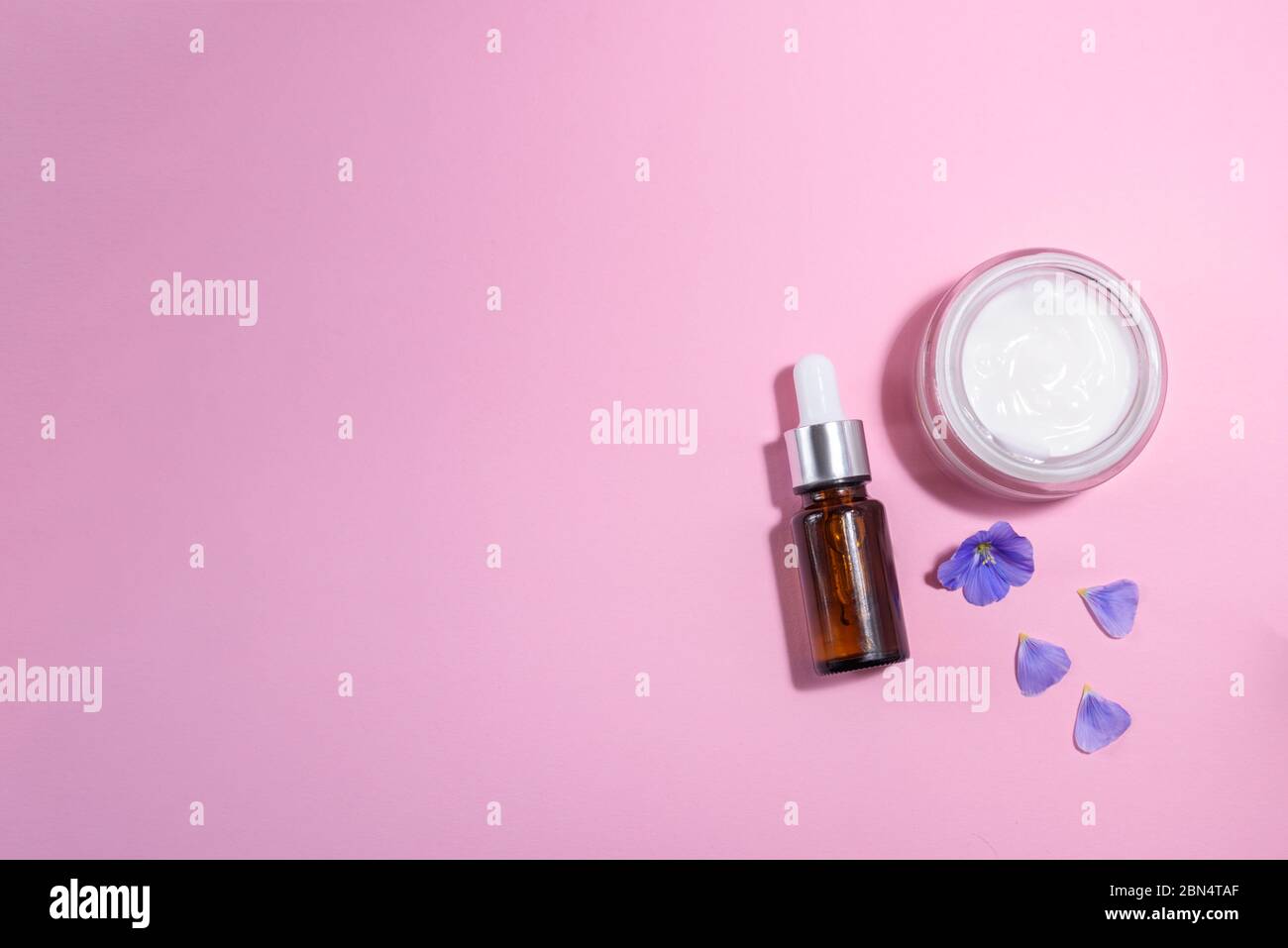 Eine Glasflasche mit Pipette mit weißer Gummispitze und Blume daneben auf dem rosa Hintergrund. Naturhaut Konzept. Bio-Spa-Kosmetik. Cl Stockfoto