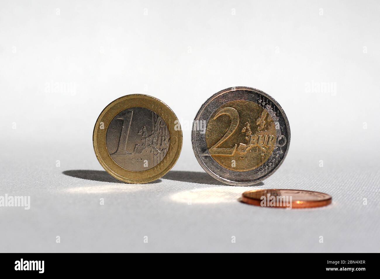 Drei Euro-Münzen auf weißer Oberfläche, zwei balancieren auf ihrer Seite. Mit besonderer Wirkung durch das Sonnenlicht. Stockfoto