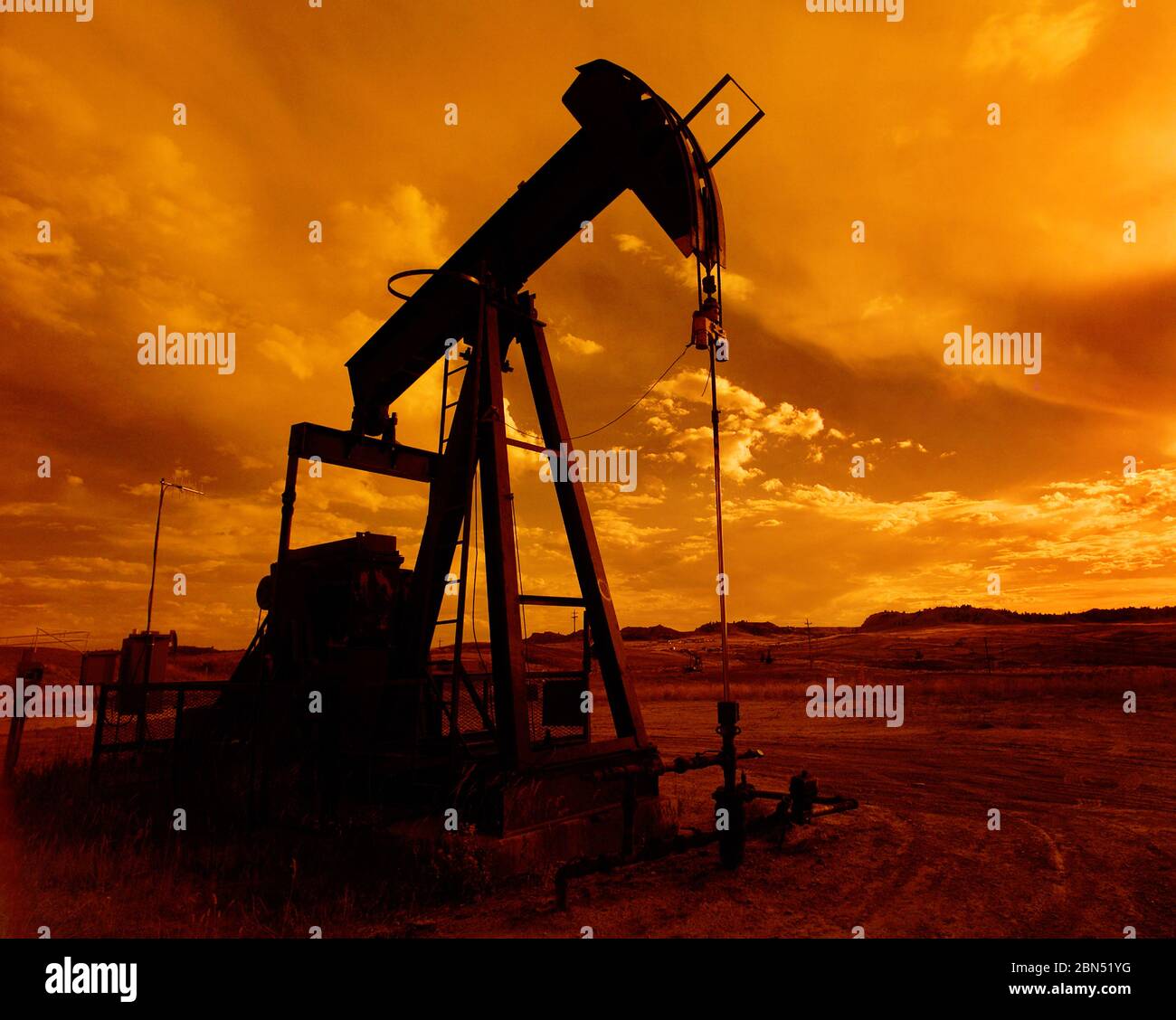 Ein Ölfeld-Pumpenheber, der bei Sonnenuntergang Öl aus dem Boden pumpt. Stockfoto