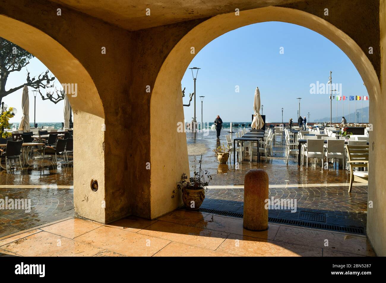 Blick auf den See von einer gewölbten Veranda in der Altstadt von Garda mit leerem Café im Freien an einem windigen Tag mit hohen Wellen, die die Straße überfluten, Verona, Italien Stockfoto