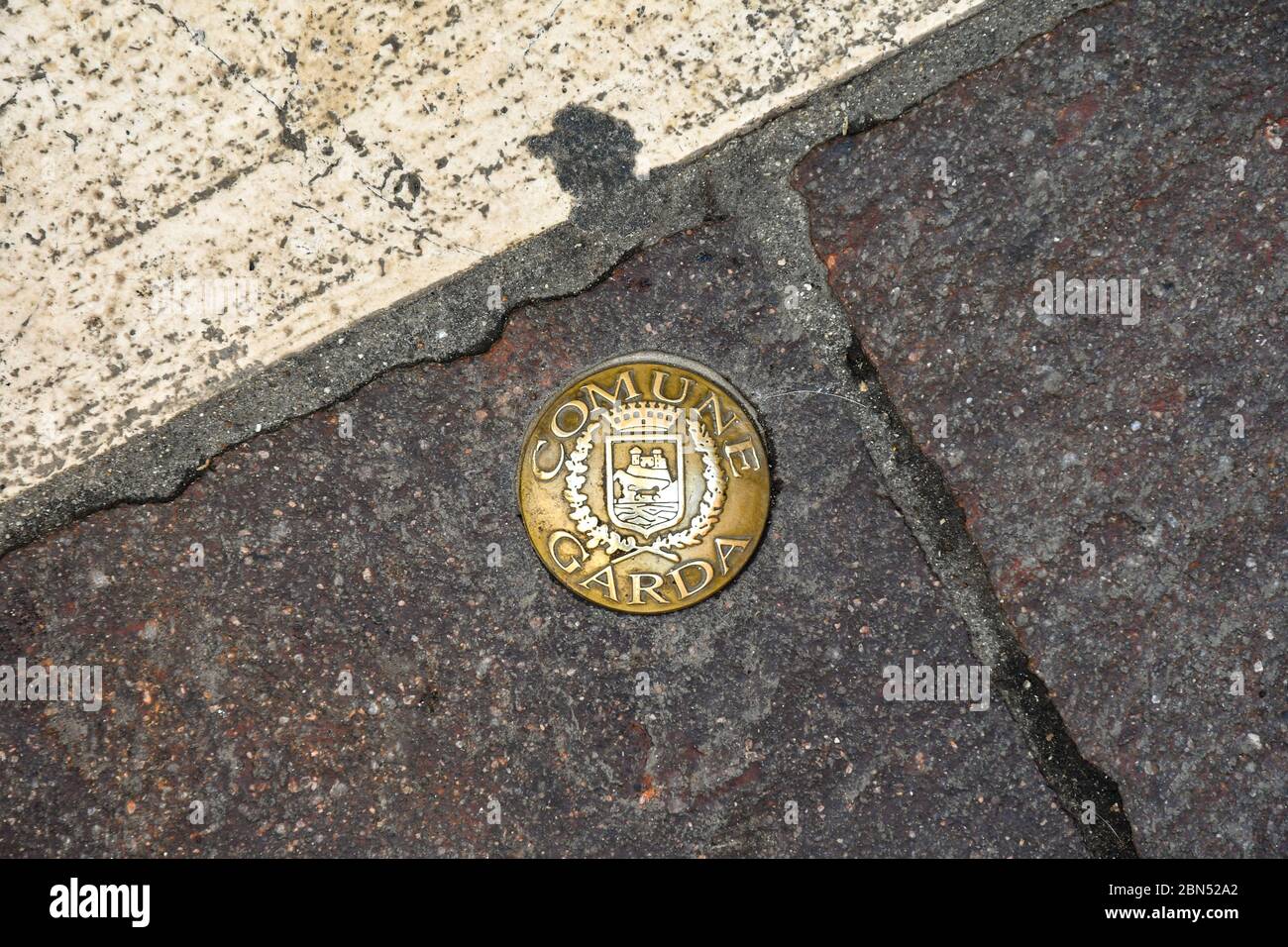 Hohe Winkel Nahaufnahme eines goldenen Gusseisenkreises mit dem Stadtmantel der Altstadt von Garda auf einem Straßenpflaster, Verona, Venetien, Italien Stockfoto