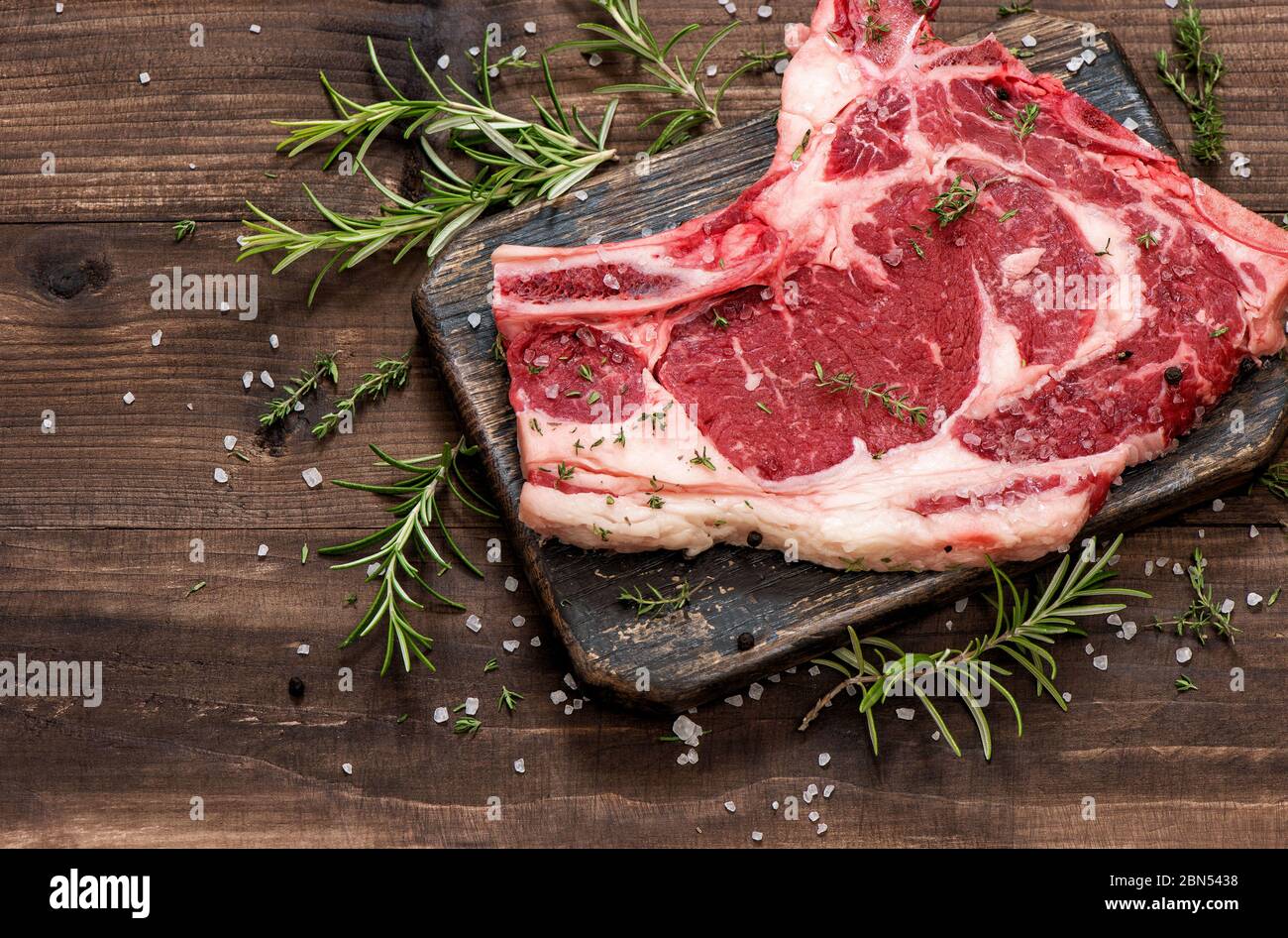 Rohes Rindfleisch mit Kräutern und Gewürzen auf Holzbrett. Hintergrund der Speisen Stockfoto
