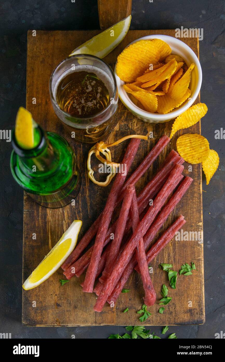 Trockene Lachssticks mit Bier, Zitrone und Kartoffelchips auf dunklem ...