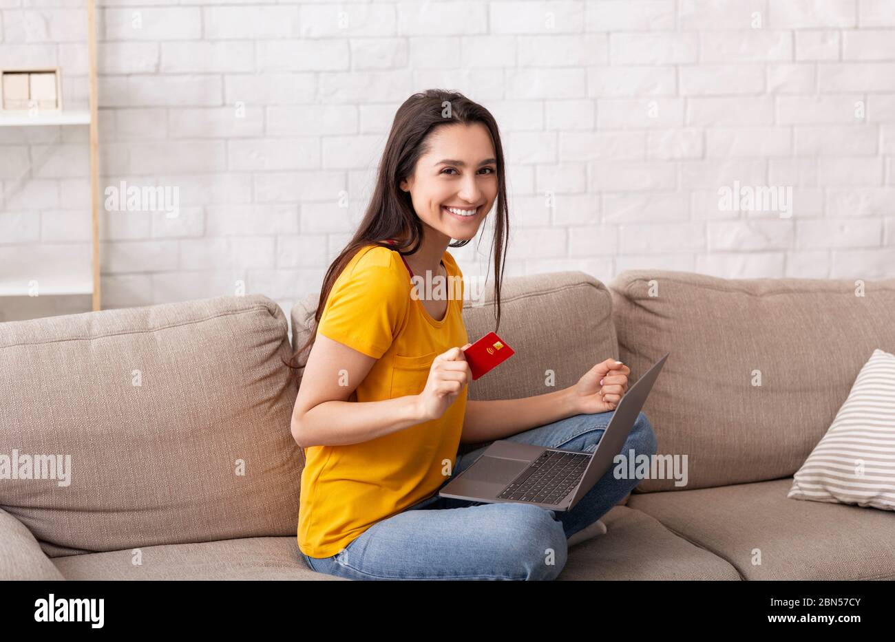 Einkaufen zu Hause. Hübsches Mädchen mit Kreditkarte und Laptop kaufen Waren online, drinnen Stockfoto