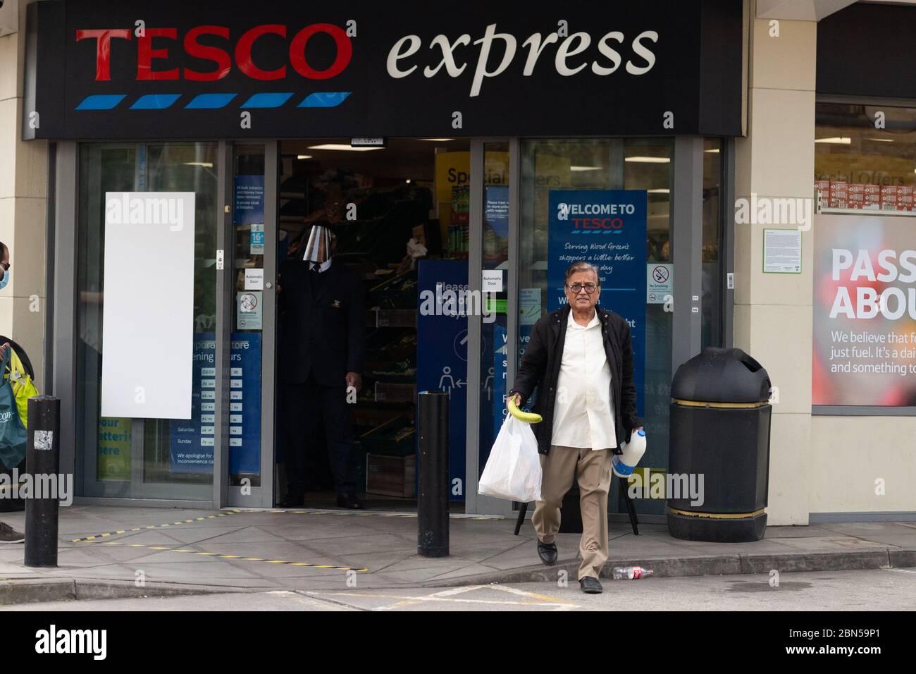 Asian man verlässt Tesco Express Supermarkt am Ostersonntag, mit wesentlichen Artikeln. Stockfoto